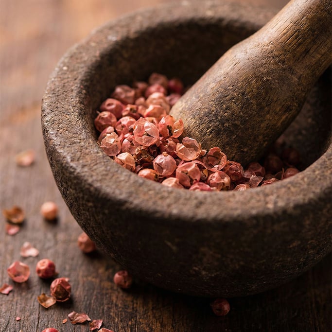 Pink peppercorns in a small stone mortar, their papery rose-pink shells catching soft light