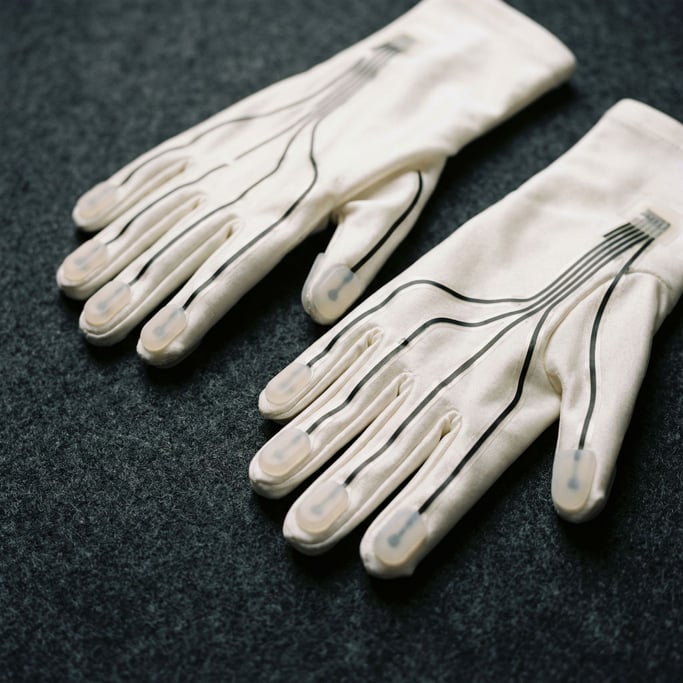 A pair of haptic gloves in pearl white with thin sensor lines running along each finger