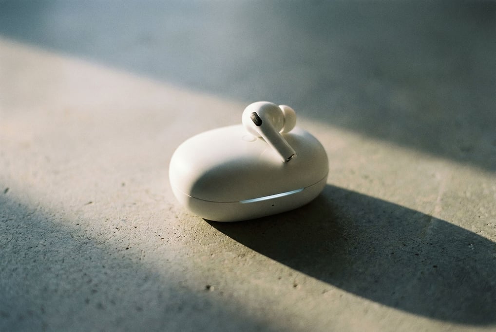 A pair of wireless earbuds in matte white rest in their charging case on a concrete surface