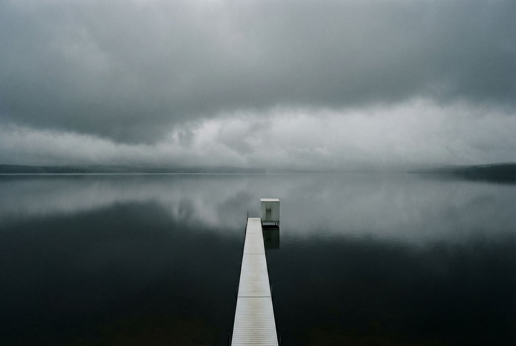 A glass-still lake reflecting a sky of low grey clouds