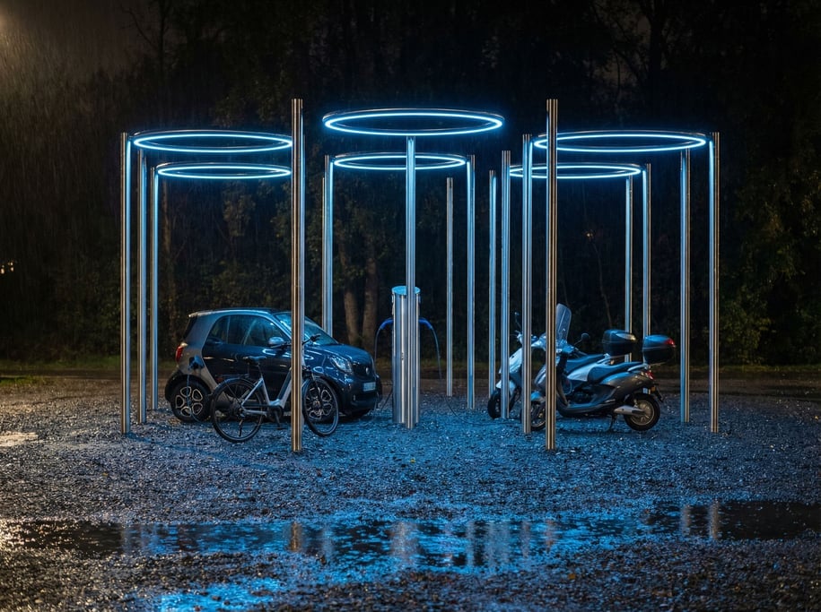 A charging station for personal vehicles resembles a minimalist sculpture garden — tall thin chrome