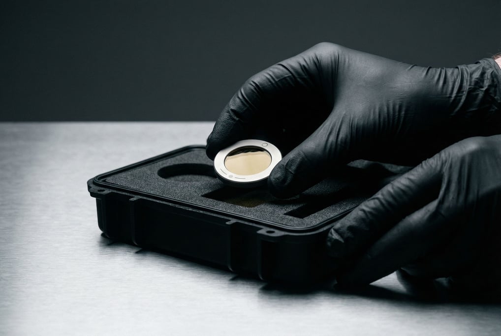 A technician in black nitrile gloves carefully inserts a small disc — titanium with a gold-tinted gl