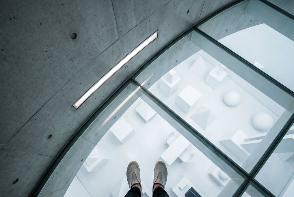 A curved concrete wall meeting a glass floor that reveals a level below — a pristine white room with