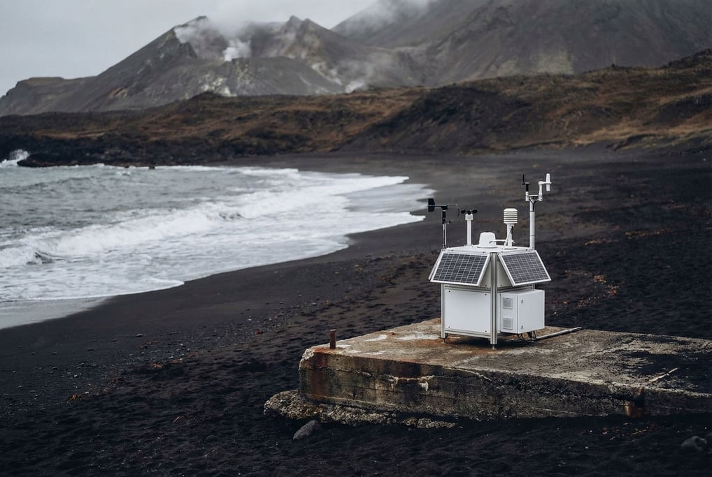 A volcanic black sand beach with a modular weather station on a concrete platform