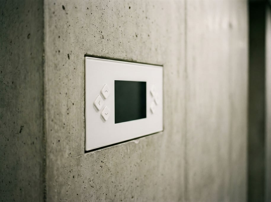 A wall-mounted control panel with a dark screen and four physical buttons arranged in a diamond patt