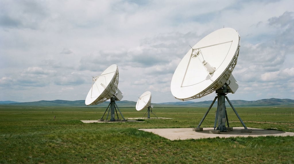 A satellite ground station in a remote grassland — three white dish antennas of different sizes poin