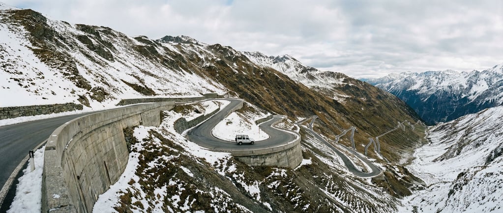 An ultra-wide panorama of a mountain pass road carved into the mountainside