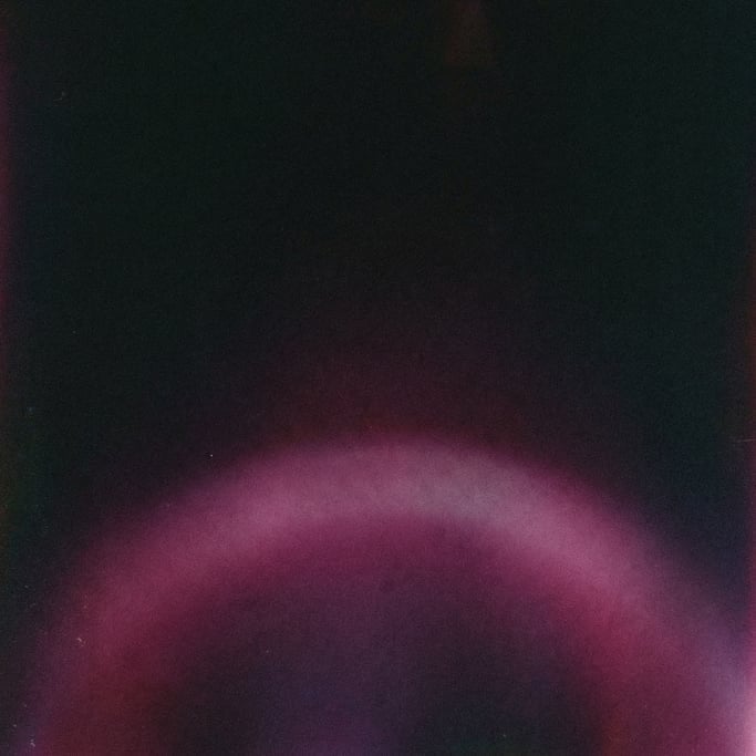 Moody film grain gradient, near-black background with a diffused arc of deep magenta light sweeping