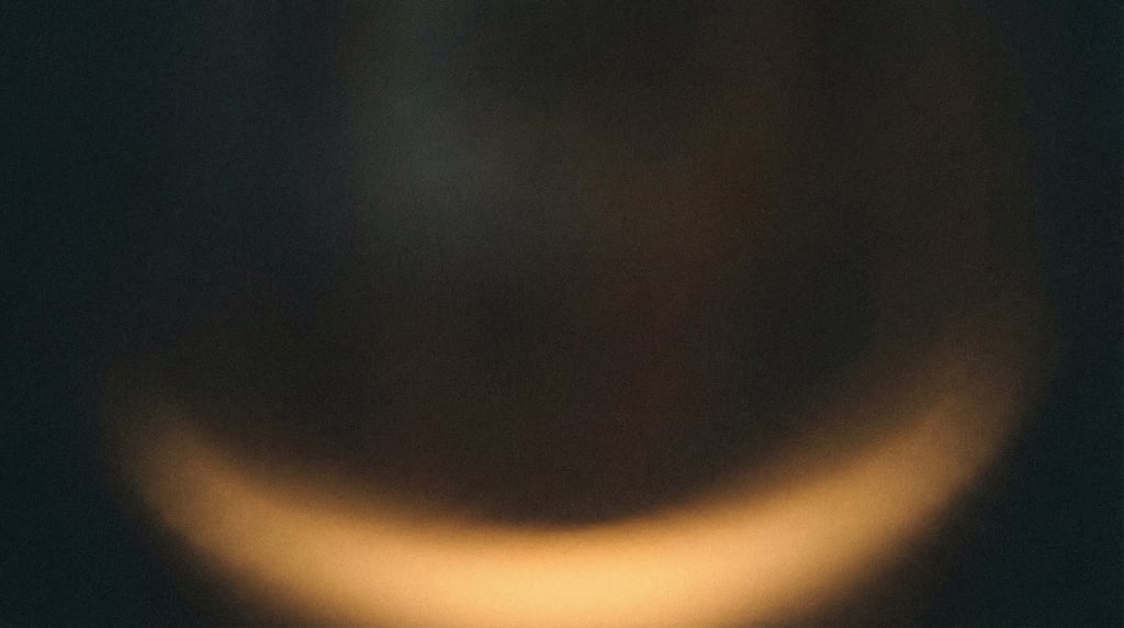 Dark grainy gradient, charcoal canvas with a single soft crescent of warm marigold light along the b