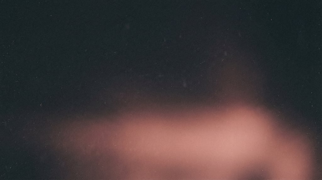 Moody film grain gradient, charcoal background with a wide diffused pool of warm rose light along th