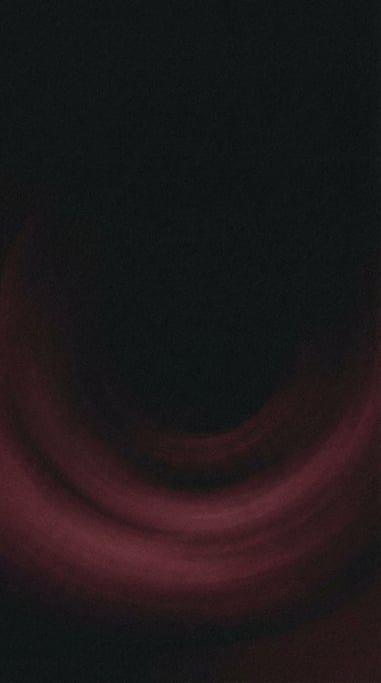 Dark grainy gradient abstract, black canvas with a soft sweeping arc of deep wine red across the low