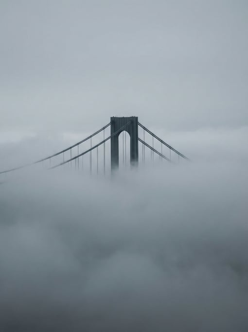 Only the cables and tower tops pierce the fog — a suspension bridge in thick atmospheric haze