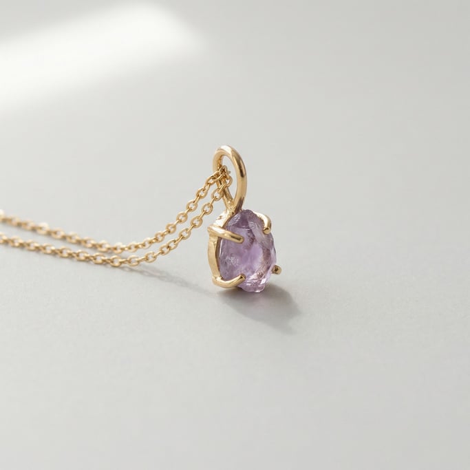 Delicate gold pendant necklace featuring a tiny raw amethyst stone set in a minimal claw setting