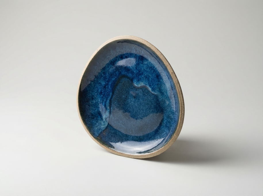 Decorative ceramic dish in an organic pebble shape with a pooling reactive blue glaze and raw clay u