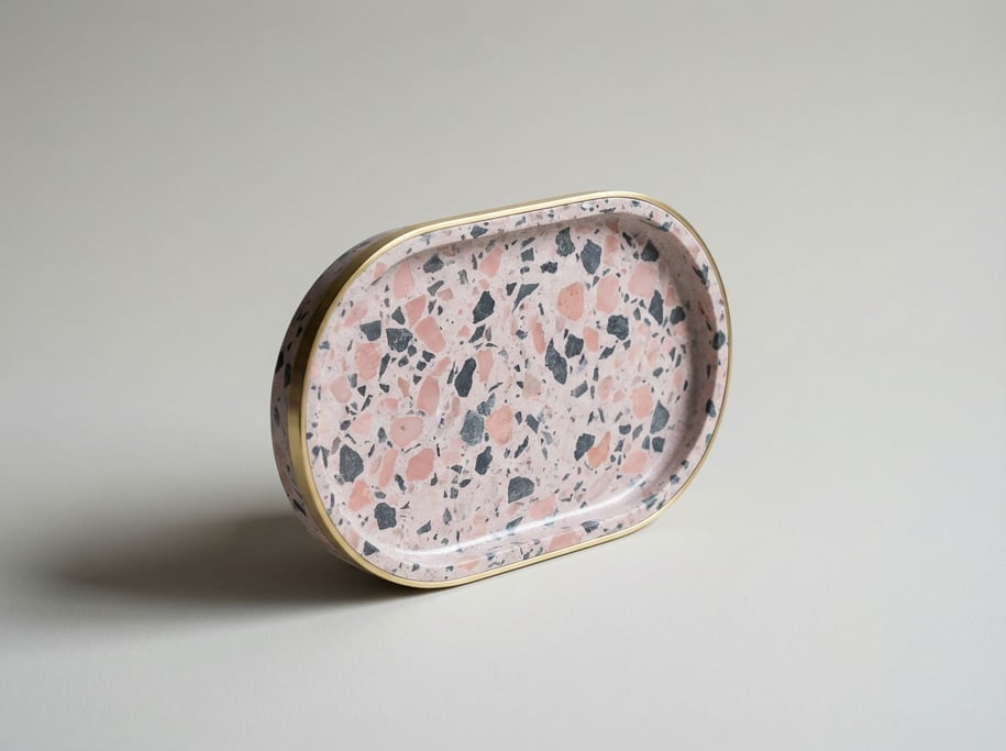Terrazzo trinket tray in pink and grey aggregate chips with a polished surface and a thin brass rim