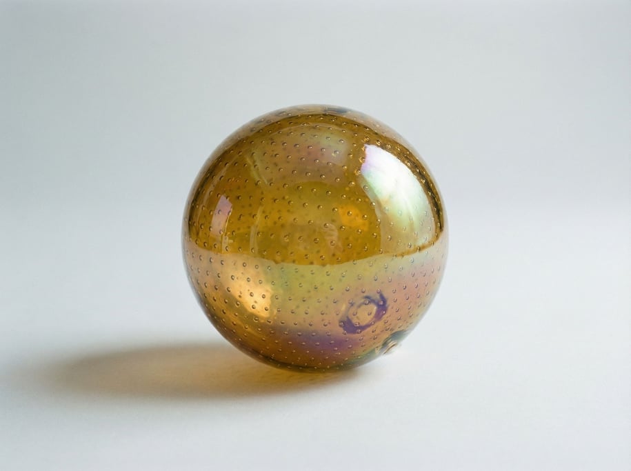 Hand-blown glass sphere ornament in iridescent amber with shifting color and tiny trapped air bubble