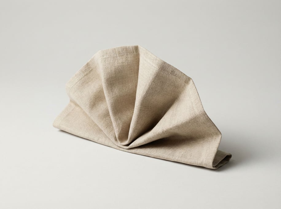 Linen table napkin folded into a precise architectural fan shape in natural oat-colored Belgian line
