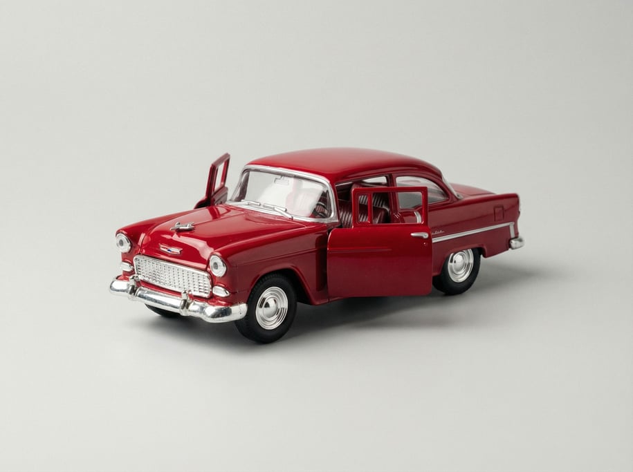 Die-cast vintage toy car in cherry red enamel paint with chrome bumpers, rubber tires