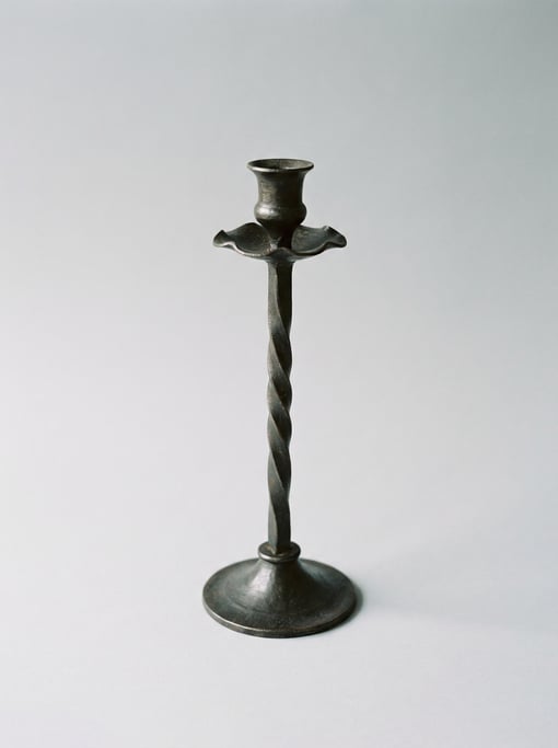 Tall wrought iron taper candle holder with a twisted stem design, drip-catching bobeche