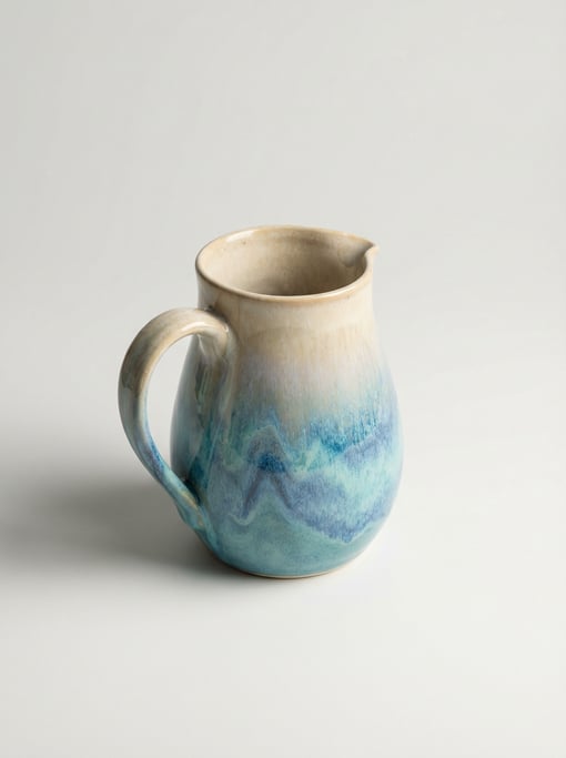 Stoneware pitcher in reactive drip glaze shifting from warm cream to ocean blue with a comfortable p