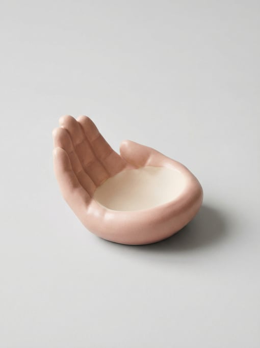 Ceramic ring dish shaped like a cupped open palm in matte blush pink glaze with a smooth interior su