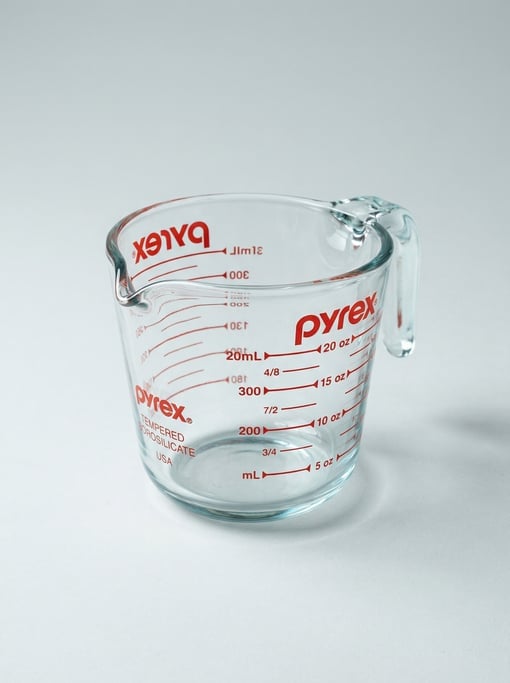 Glass measuring cup with red screen-printed graduated markings in milliliters and ounces on thick te
