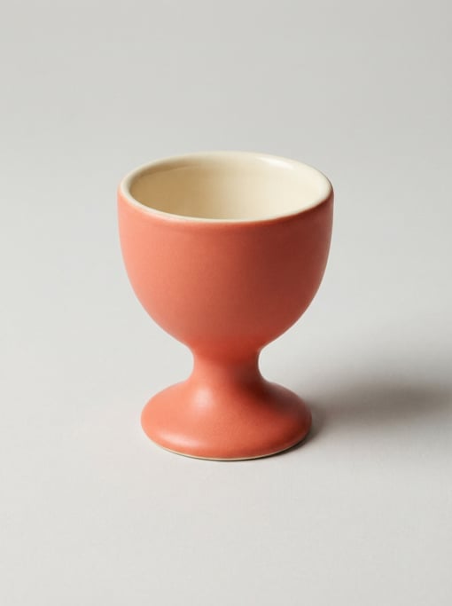Ceramic egg cup in matte coral glaze with a glossy cream interior, a narrow pedestal stem