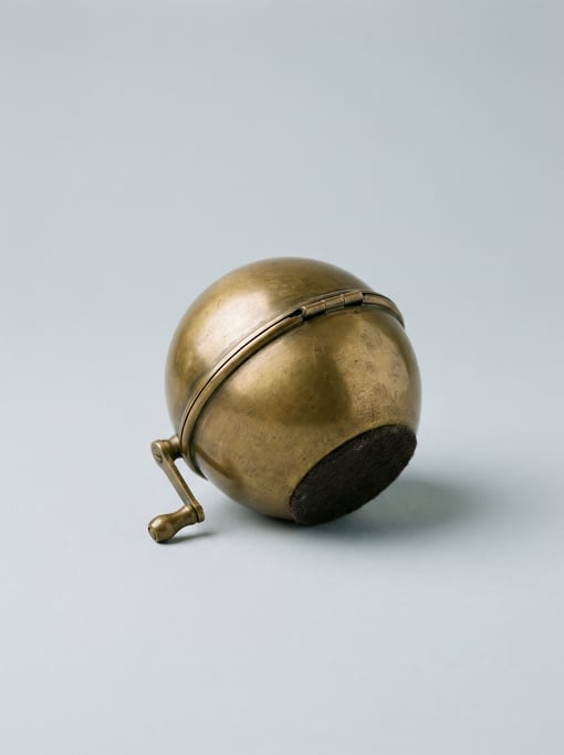 Globe-shaped pencil sharpener in antique brass with a tiny hand-crank mechanism, hinged equator