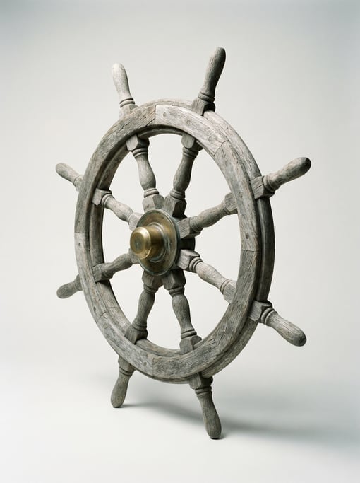 Antique ship wheel in weathered grey teak wood with eight turned spokes, brass hub cap
