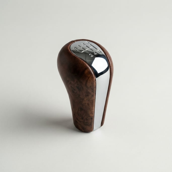 Leather-wrapped gear shift knob in dark walnut burl with a chrome insert showing an engraved six-spe