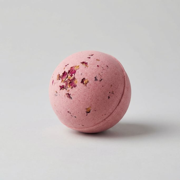 Spherical bath bomb in dusty rose pink with dried rose petal fragments embedded across the surface a