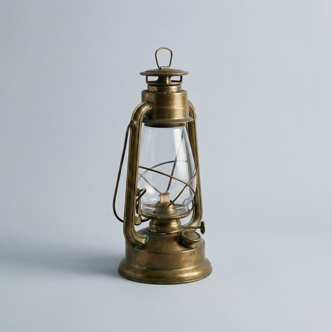Hurricane lamp in aged brass with a clear glass chimney, wire handle, adjustable wick wheel