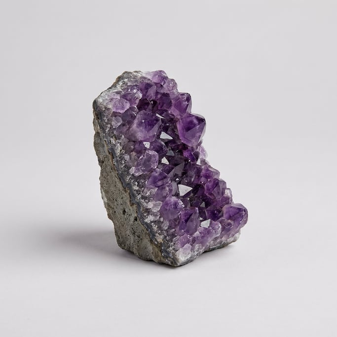 Raw amethyst crystal cluster with deep purple prismatic points emerging from a rough grey volcanic m