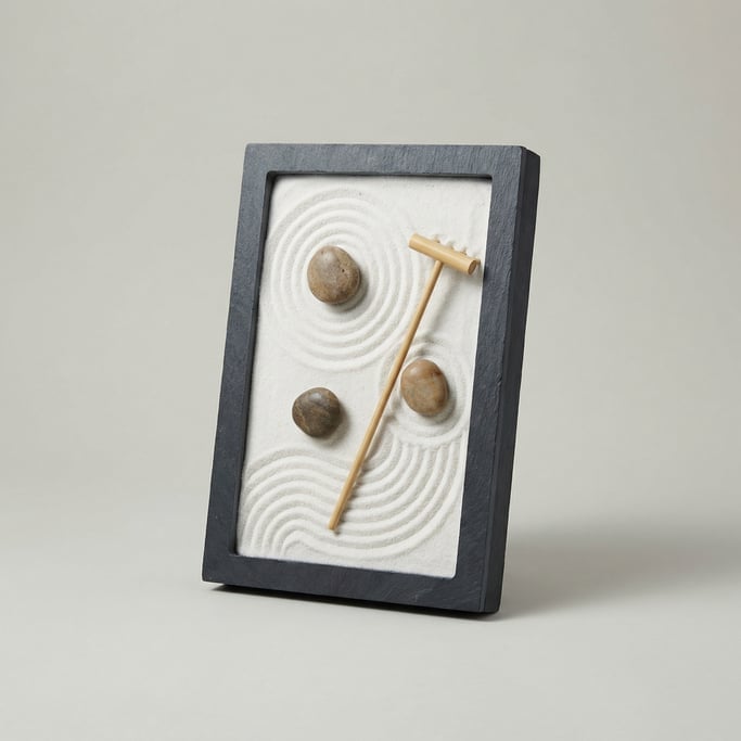 Tabletop zen garden tray in dark slate stone with white raked sand, three smooth river pebbles
