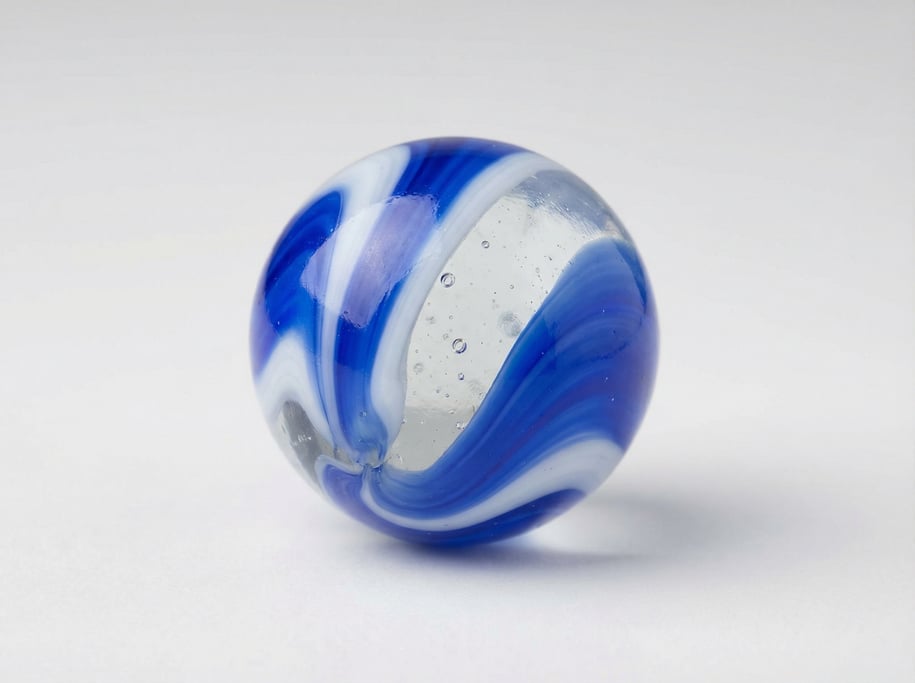 Glass marble in swirled cobalt blue and white with a clear transparent core and tiny internal air bu