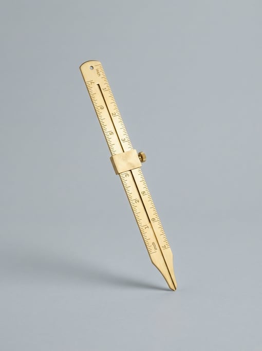 Brass hem gauge ruler in polished gold with a sliding marker, engraved measurements in inches