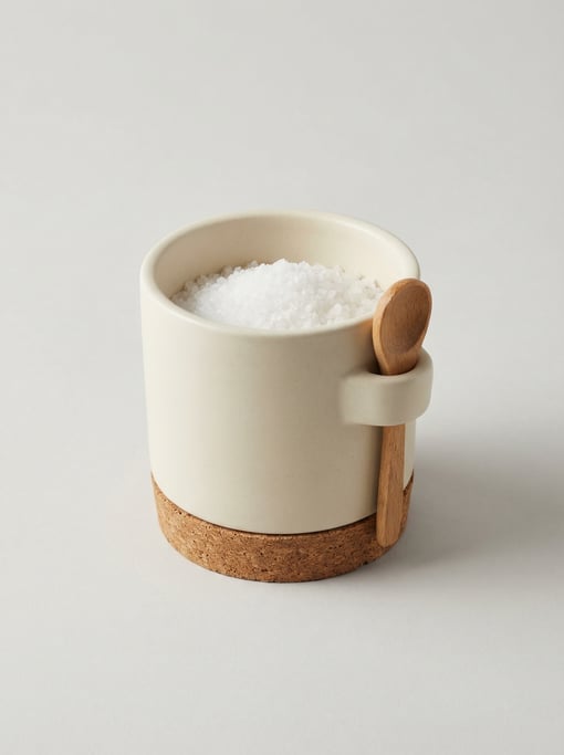 Ceramic salt cellar in matte cream stoneware with a wide open top, a small wooden spoon rest