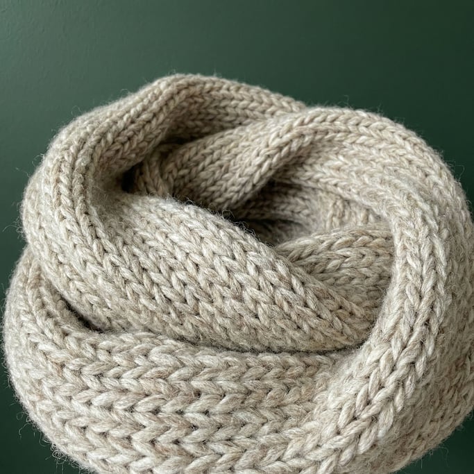 Chunky knit infinity scarf in heathered oatmeal wool, draped in a loose coil and filling the frame