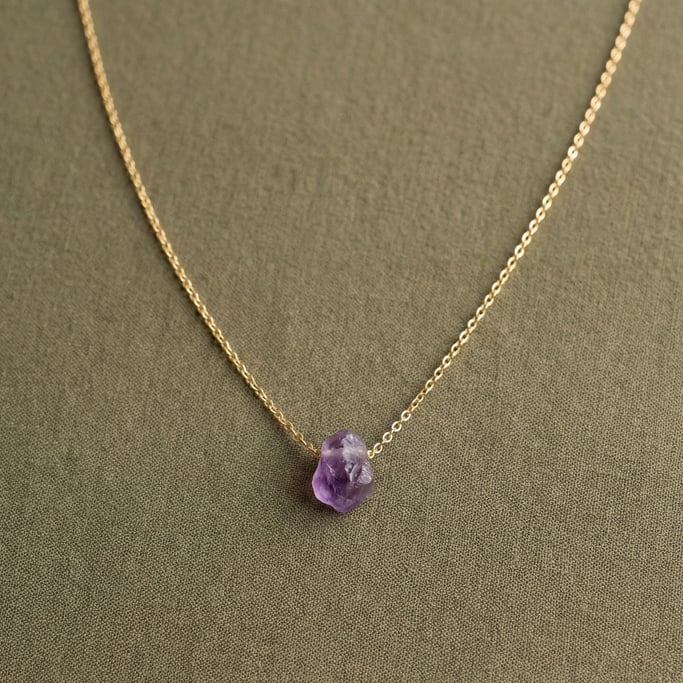 Delicate gold pendant necklace with a tiny raw amethyst stone, draped in a gentle curve