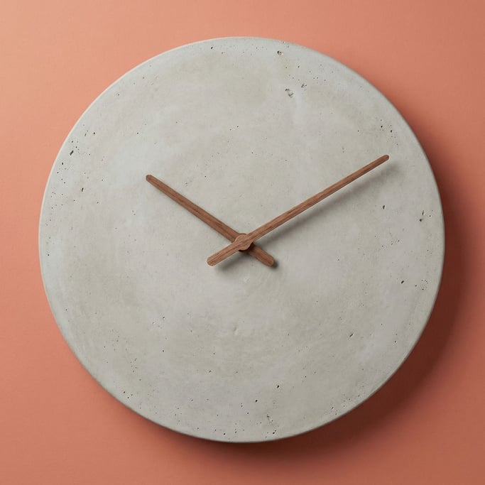 Minimalist concrete wall clock with walnut wood hands and no numerals, soft overhead light