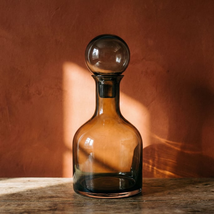Smoked glass carafe with a spherical stopper, light passing through and creating subtle caustics