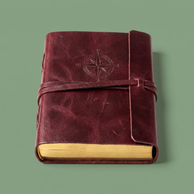 Leather-bound journal in rich burgundy with gold foil page edges, soft overhead studio light