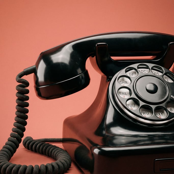 Bakelite rotary telephone in glossy black with a coiled fabric cord, two-point studio lighting
