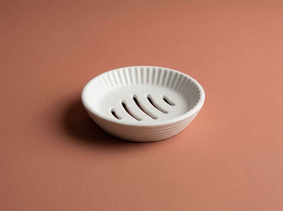 Ceramic soap dish in ribbed white porcelain with drainage channels, soft studio fill light