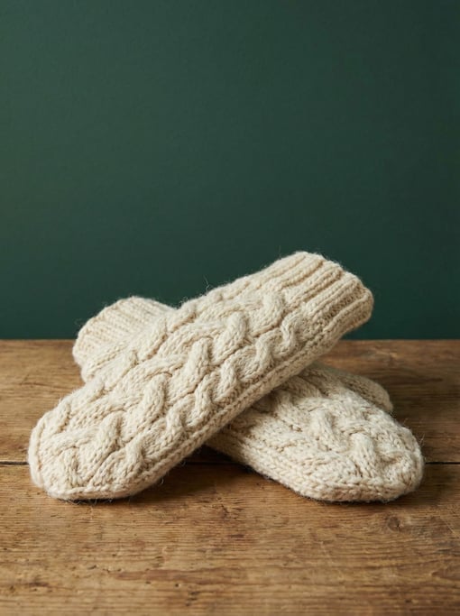 Hand-knitted wool mittens in cream cable-knit pattern, arranged overlapping