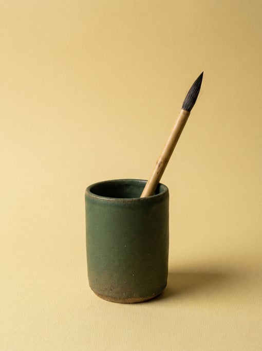 Ceramic pen cup in matte forest green holding a single calligraphy brush