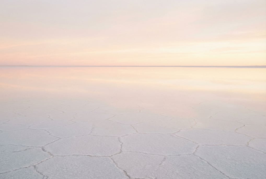 White salt flats stretching to the horizon, hexagonal crack patterns under a cloudless sky