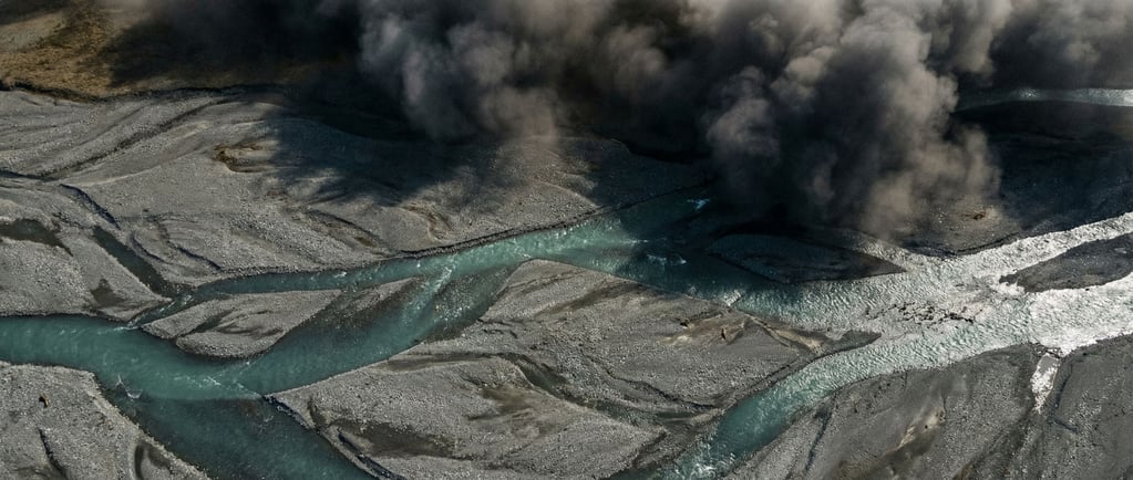 Turquoise glacial meltwater river braiding across a gray gravel plain, seen from above