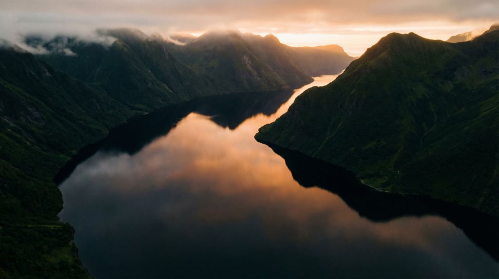 Fjord at dawn, dark mirror-still water stretching between steep green mountains disappearing into mi