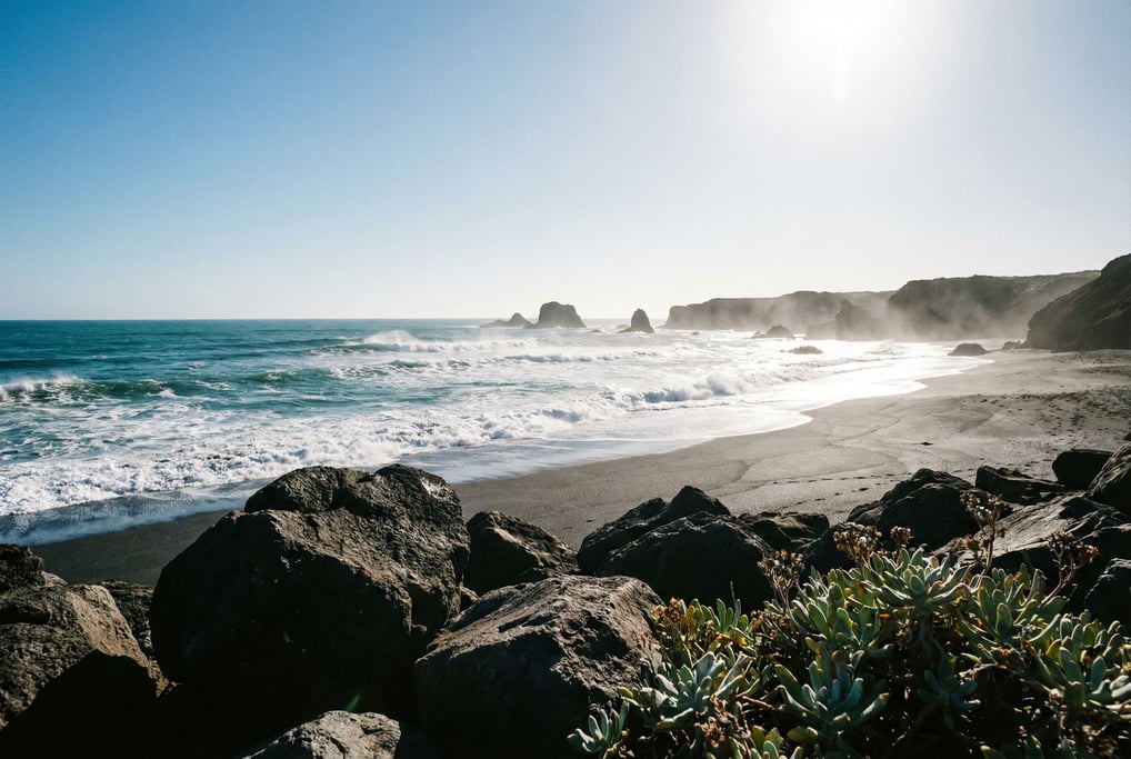 Volcanic black sand beach with turquoise waves breaking on shore, stark contrast of dark and bright